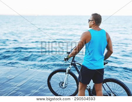 Back View Of Athletic Sexy Man With Bicycle Outdoors At Seaside.