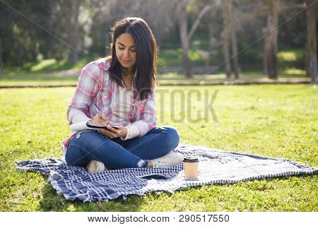 Positive High School Student Making Draft Of Essay In Park. Beautiful Girl In Casual Sitting On Gras