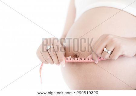 Mid-section of pregnant woman measuring her belly with pink measure tape