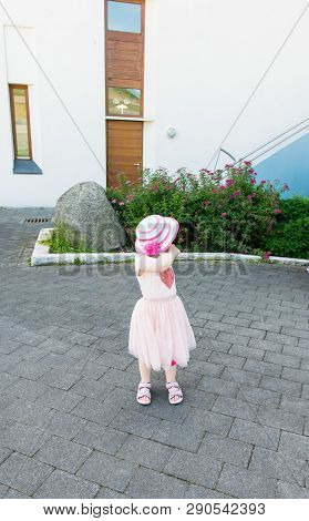 The Little Girl In A Pink Dress And A Hat Walks On The Summer City And Is Photographed At The Moment