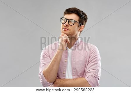 education, wisdom and people concept - thinking young man in glasses over grey background