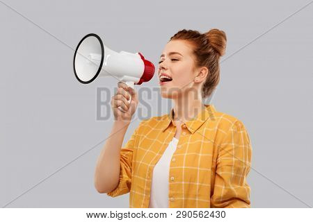 communication, feminism and rights concept - red haired teenage girl in checkered shirt speaking to megaphone over grey background