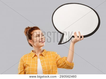 people concept - smiling red haired teenage girl in checkered shirt holding blank speech bubble over grey background