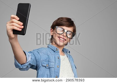 Cute Boy In Damaged Glasses Smiling And Posing For Selfie Against Gray Background