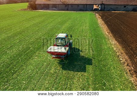 Unrecognizable Farmer In Agricultural Tractor Is Fertilizing Wheat Crop Field With Npk Fertilizers, 