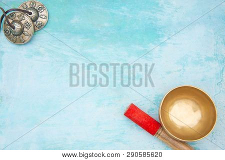Light Blue Hand Made Background With Accessories For Meditation. Bronze Singing Bowl With A Red Stic