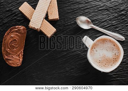 A Piece Of Bread, A Mug Of Coffee And A Waffle, Smeared With Chocolate Paste, On A Black Textured Ba