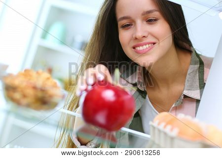 Portrait Of Female Standing Near Open Fridge Full Of Healthy Food, Vegetables And Fruits. Portrait O