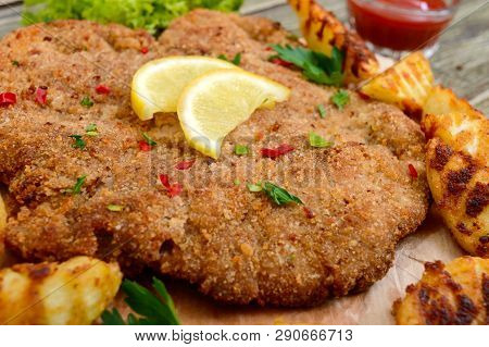 Large Schnitzel With Baked Golden Potatoes On A Wooden Cutting Board. Wiener Schnitzel.