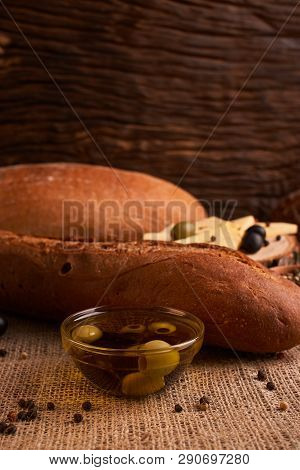 Fresh Bread Baguette With Olive Oil, Olives. Cheese And Rosemary On Wooden Background. Teasty Breakf