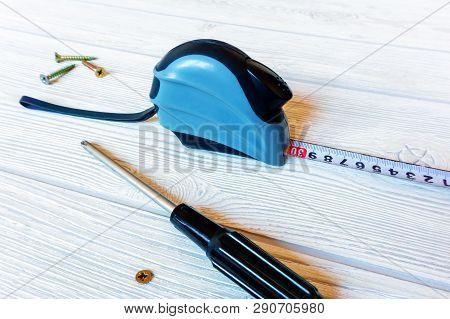 Metric Self-retracting Metal Tape Measure, Screwdriver And Screws On A Light Wooden Surface