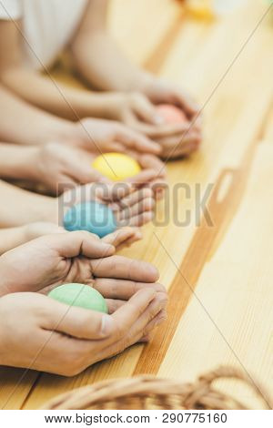 Four Colored Easter Eggs In Mother Father Sister And Brothers Hands Like In The Nests. Blurred Backg