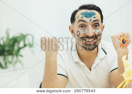 Funny Smiling Young Father Wuth Painted Face And Hands Looking At The Camera, Demonstrating His Holi