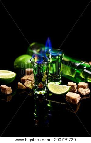 Absinthe Poured Into A Glass. Absinthe In Glass With Lime Slices On Dark Background. Cube Brown Suga