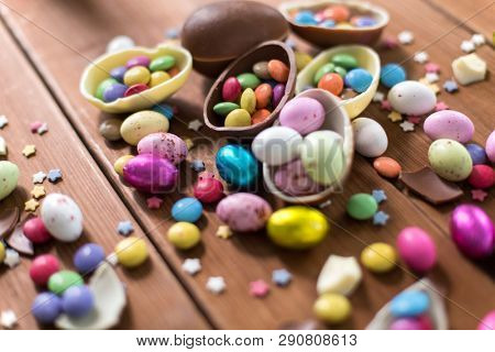 easter, sweets and confectionery concept - chocolate eggs and candy drops on wooden table