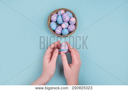 Woman Hands Holding Dyed On Blue, Pink And Violet Easter Eggs In The Straw Basket Isolated On Blue B