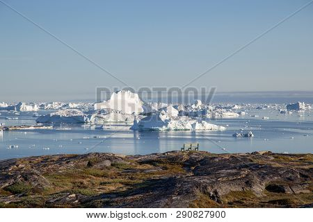 Ilulissat, Greenland - July 9, 2018: A Bench At The Coastline With Iceberg View. Rodebay, Also Known
