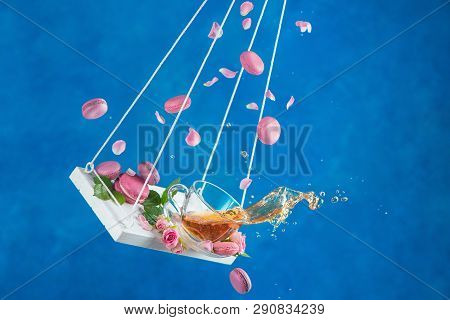Rose Tea With Macaron Cookies And Pink Flower Petals On Swings In Motion. Action High Speed Photogrp