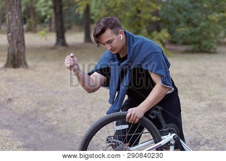 Young Causacian Man With Screwdriver Tries To Damage The Bicycle Wire At The Abandoned Park. Vandal 