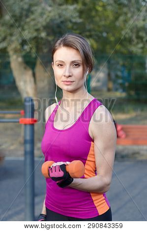 Beautiful Slim And Sporty Girl In Bright Sportswear Trains With Dumbbell For Biceps At Outdoor Sport