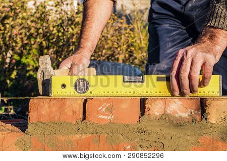 Bricklayer Checks The Horizontal Level Of Brick Masonry Wall With A Bubble Level And And Lacing Cord