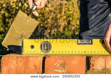 Bricklayer Checks The Horizontal Level Of Brick Masonry Wall With A Bubble Level And And Lacing Cord