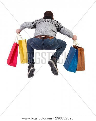 Back view of a jumping man in a sweater with shopping bags that runs.   Rear view people collection. Isolated over white background. A guy in a warm sweater with shopping bags happily bounced up.