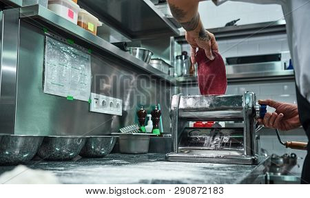 Making Pasta. Cropped Image Of Male Chef Rolling A Knead Through Pasta Machine While Working In Rest
