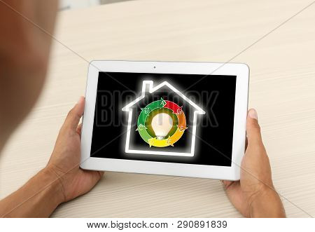 Man Using Tablet With Icon Of Energy Efficiency And Lamp Bulb On Screen At Table, Closeup