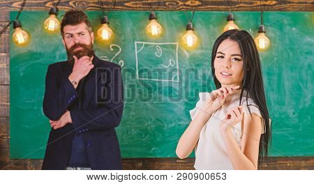 Man With Beard And Young Lady Teacher Stand In Classroom, Chalkboard On Background. Lady Teacher And