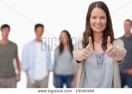 Thumbs up dato da donna sorridente con gli amici dietro di lei contro uno sfondo bianco