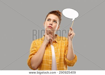 photo booth, party props and people concept - red haired teenage girl in checkered shirt holding blank speech bubble and thinking over grey background