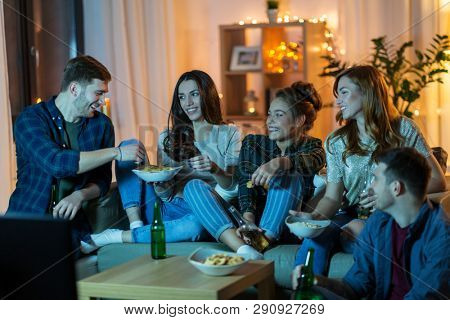friendship, and leisure concept - happy friends with non-alcoholic drinks and snacks watching tv at home in evening