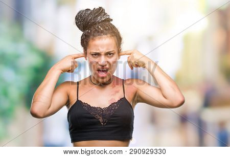 Young braided hair african american with pigmentation blemish birth mark over isolated background covering ears with fingers with annoyed expression for the noise of loud music. Deaf concept.