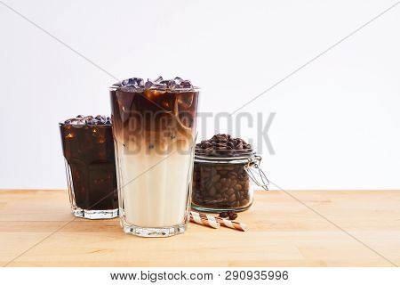 Iced Coffee And Latte Macchiato In Tall Glass With Straws And Coffee Beans In Glass Jar On Wooden Ta