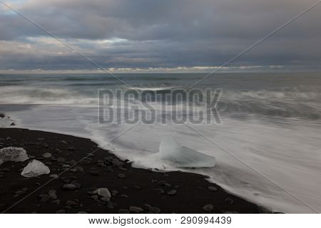 Dramatic A Sunset With Amazing Transparent Blue Iceberg Pieces On Diamond Beach With Black Sand Near