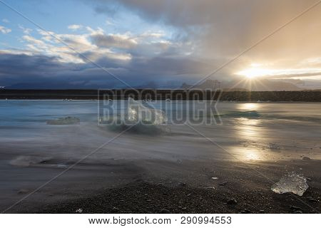 Dramatic A Sunset With Amazing Transparent Blue Iceberg Pieces On Diamond Beach With Black Sand Near