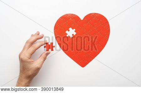 Top view of hand holding last piece near unfinished puzzle in form of heart on white background