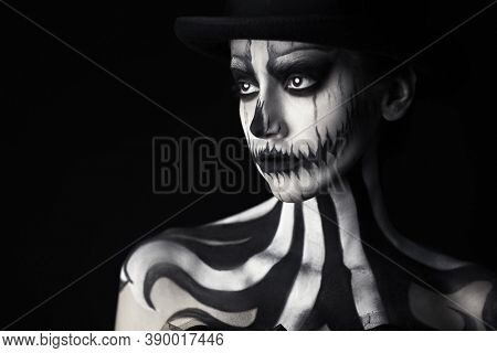 Elegant young woman in a male top-hat with pumpkin skull make-up over black background. Pumpkin queen. Costumes and makeup for Halloween. Copy space.
