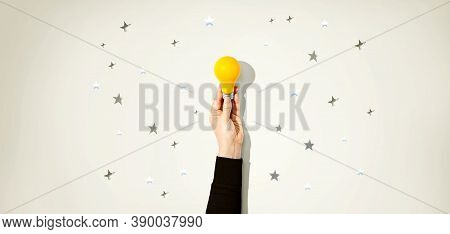 Person Holding A Yellow Light Bulb With Silver Shiny Stars