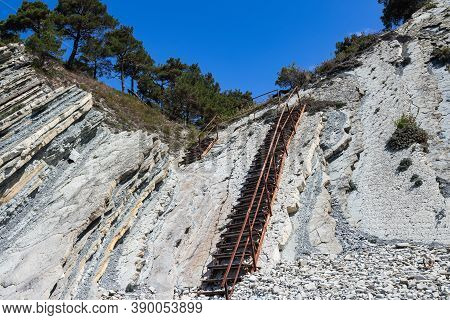 An Old Metal Staircase And Massive White Rocks On A Wild Beach. The Path To The Campsite Goes Throug