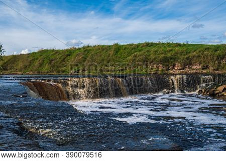 Waterfall, Water Flowing From The River Falls Down. A Stormy River With A Brown Hue.