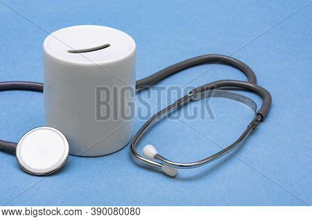 Cost Of Healthcare. Money Box With A Medical Doctors Stethoscope On Blue Background