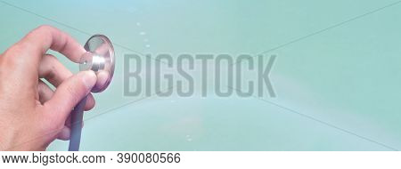 Hand Holds A Stethoscope On A Blue Background. Concept Doctor, Doctor's Appointment, Virus, Treatmen