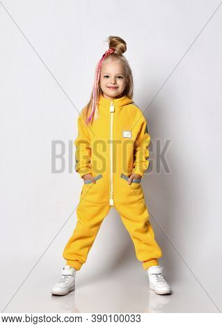 Smiling Nice Blonde Kid Baby Girl With Girlish Hairstyle And Colorful Braids In Stylish Yellow Jumps