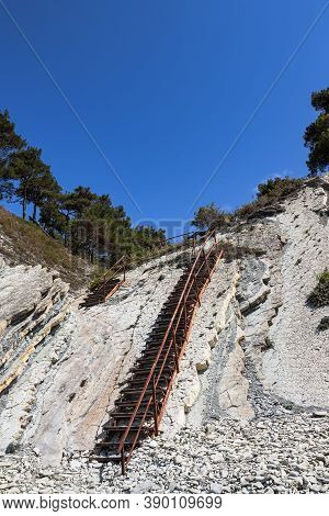 An Old Metal Staircase And Massive White Rocks On A Wild Beach. The Path To The Campsite Goes Throug