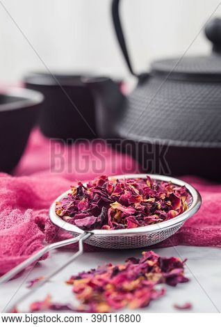 Strainer Infusor With Rose Petals Organic Tea On Red Cloth Background With Iron Teapot And Cups.