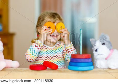 Cute Little Toddler Girl Playing Alone With Colorful Wooden Rainbow Pyramid And Toys At Home Or Nurs