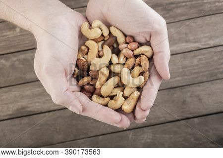 Hands Full Of Mixed Nuts Over A Wooden Background. Peanuts, Brazilian Nuts, Cashew, Baru And Almonds