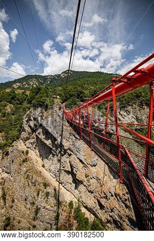 Wooden Long Footbridge Above The Deep Gorge With A River Beach At The Bottom, Between The Rocks. Wil